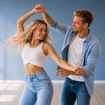 Blondes Paar tanzt lächelnd Discofox vor einem blauem Hintergrund
